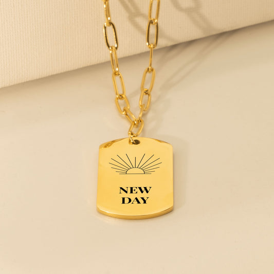 Tag pendant engraved with a rising sun and NEW DAY on a gold paperclip chain