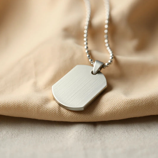 Polished engraved dog tag necklace with a fine chain laid on neutral fabric