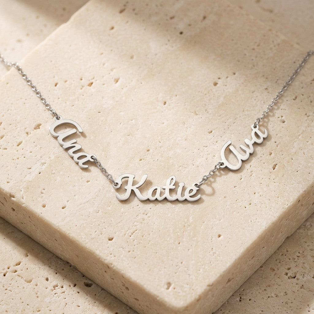 Polished steel necklace with three linked script names on a stone surface