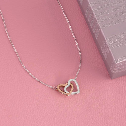 Interlocking hearts pendant on a pink background beside its box | Always Proud, Always Loved Necklace