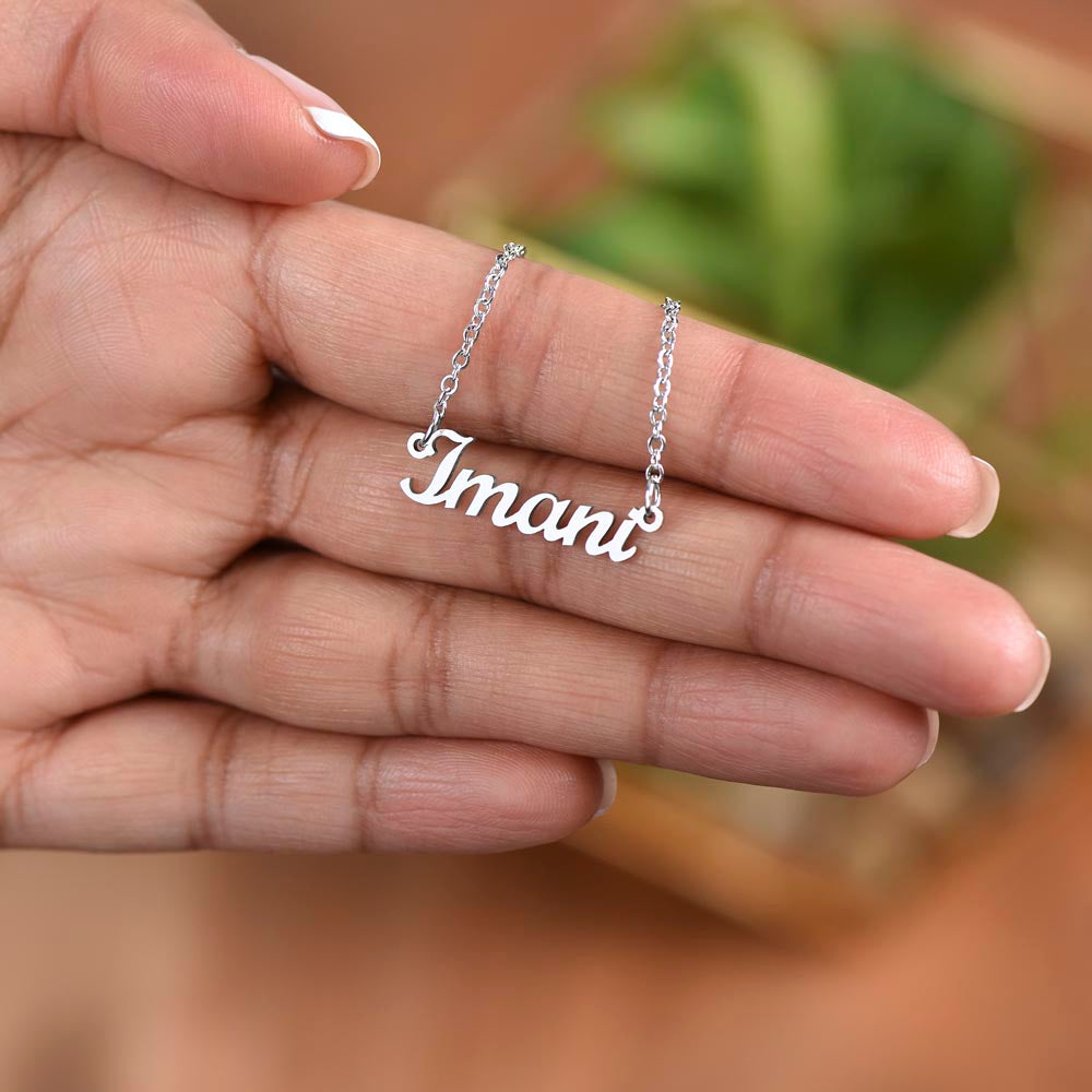 Silver name necklace held in the fingers over a plant | Chosen Name Necklace