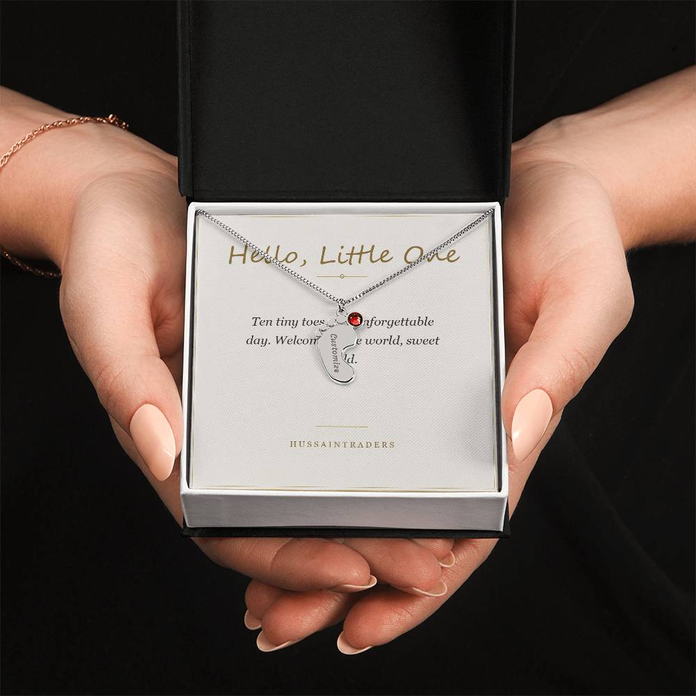 Boxed silver charm and card held in both hands | Baby Feet Birthstone Necklace
