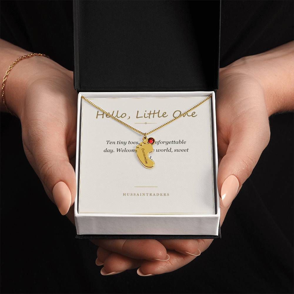 Boxed gold finish charm and card held in both hands | Baby Feet Birthstone Necklace