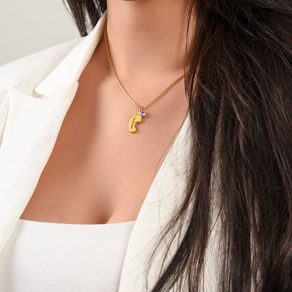 Gold finish baby feet necklace worn with a white blazer | Baby Feet Birthstone Necklace