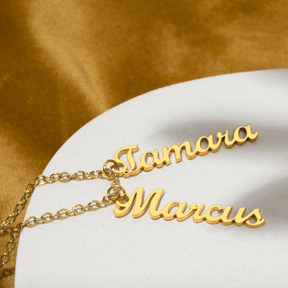 Two gold finish vertical name pendants on a gold surface | Stacked Vertical Names Necklace