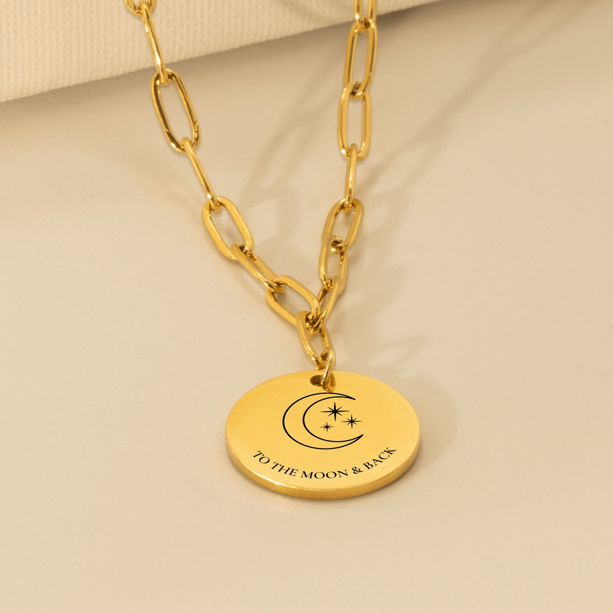 Coin pendant engraved with a crescent moon, stars and TO THE MOON & BACK on a gold paperclip chain