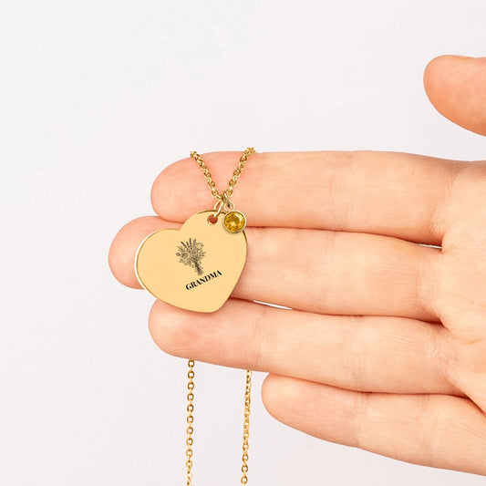 Heart pendant engraved with a flower bouquet and GRANDMA with a birthstone charm, held in a hand