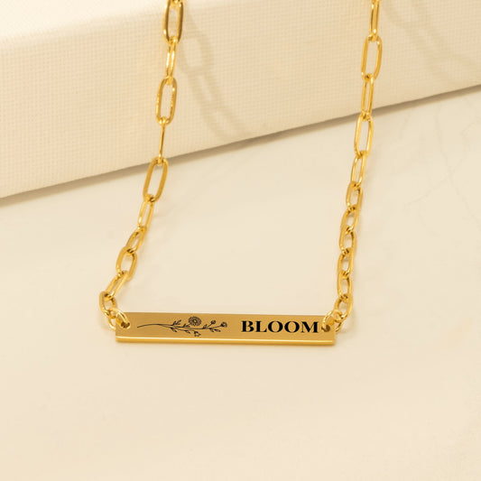 Horizontal bar engraved with a wildflower sprig and BLOOM on a gold paperclip chain