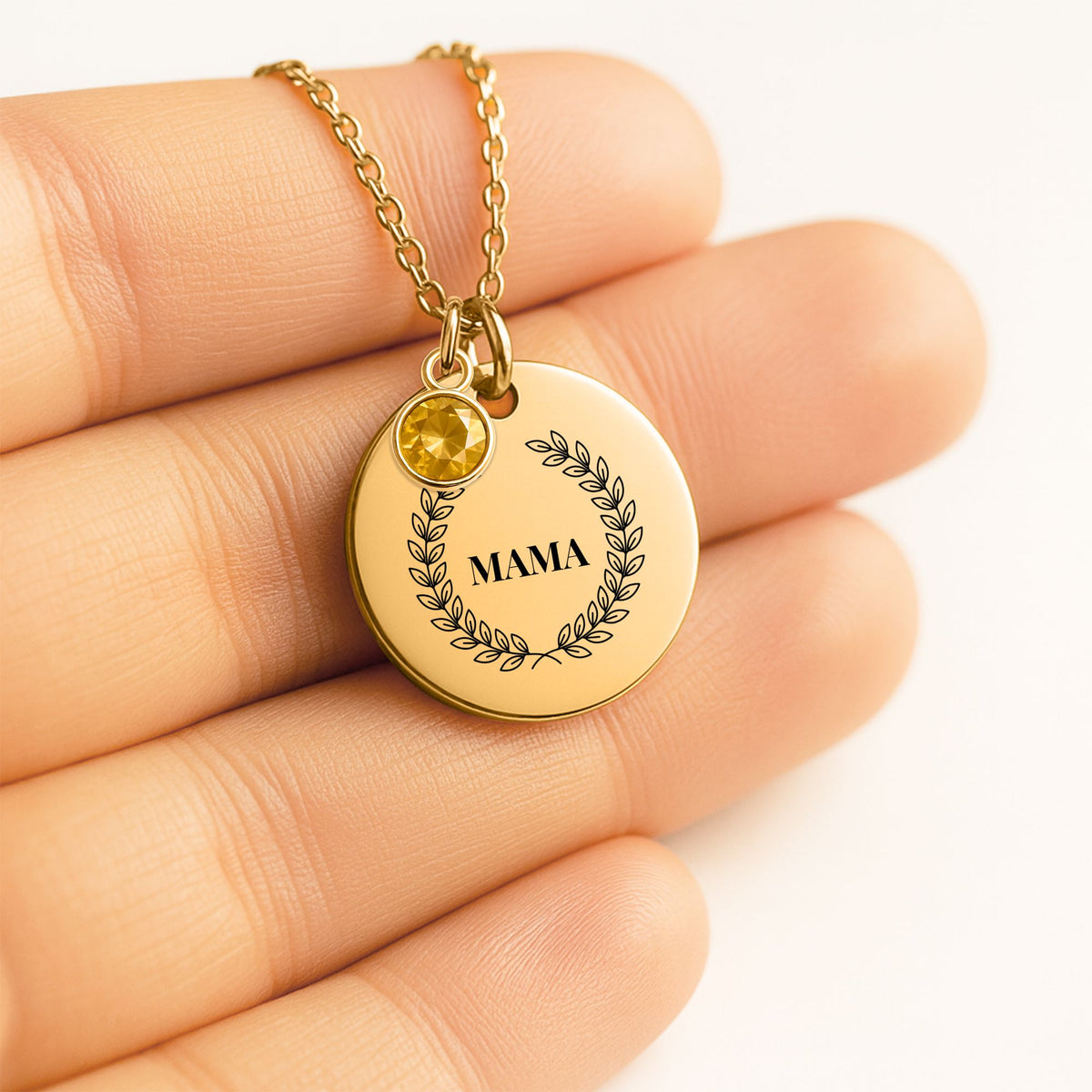 Coin pendant engraved with a laurel wreath and MAMA with a birthstone charm, held in a hand