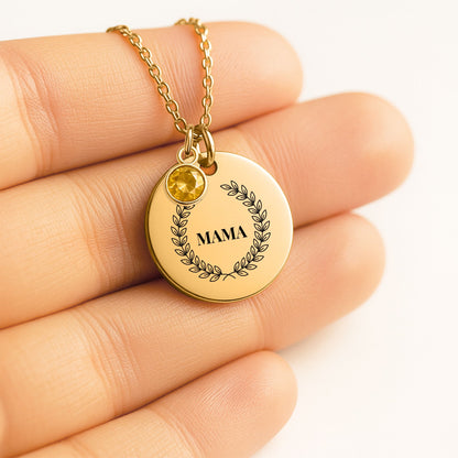 Coin pendant engraved with a laurel wreath and MAMA with a birthstone charm, held in a hand