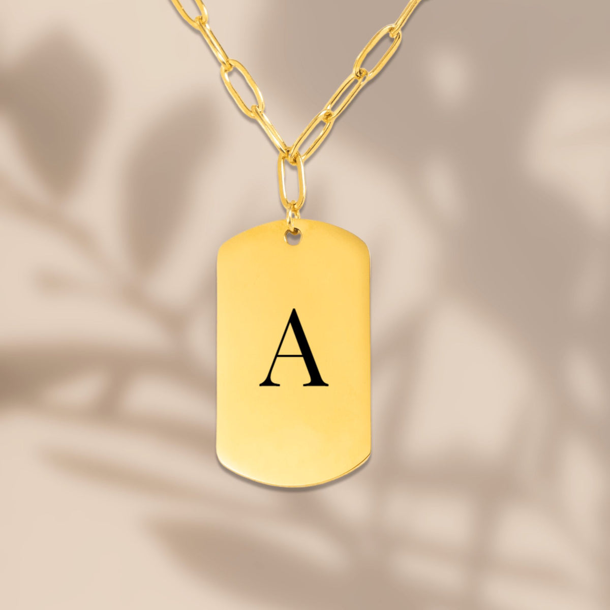 Engraved initial tag on a paperclip chain in soft window light