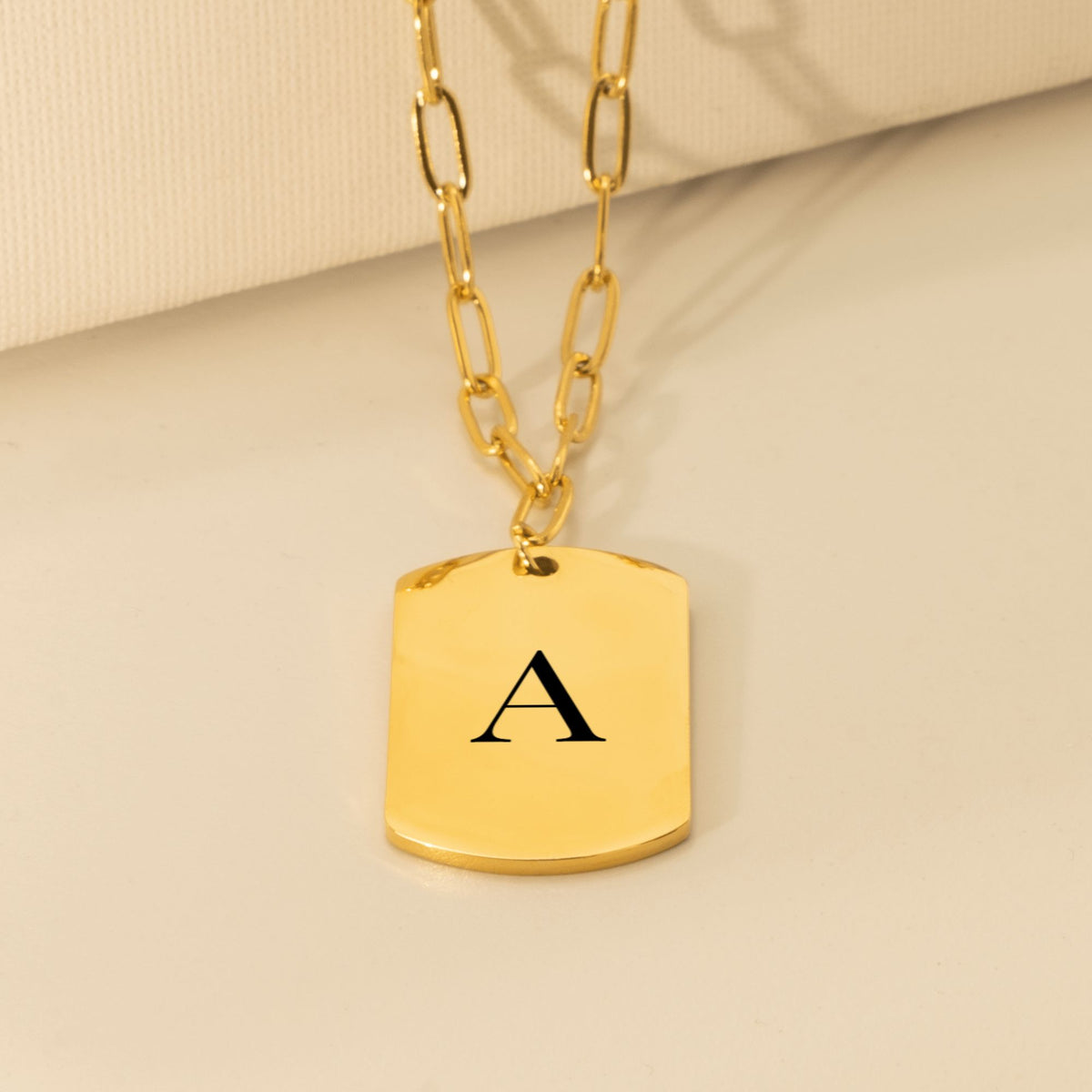 Gold tag pendant engraved with a large serif initial A on a paperclip chain