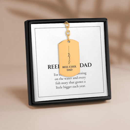 Reel Cool Dad fishing tag keychain in gold on its printed message card in a black gift box
