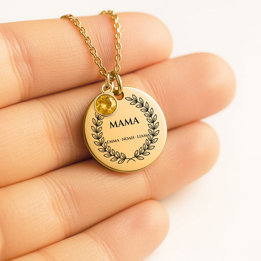 Close-up of the gold coin engraved with a laurel wreath, MAMA and sample kids' names, with a birthstone charm