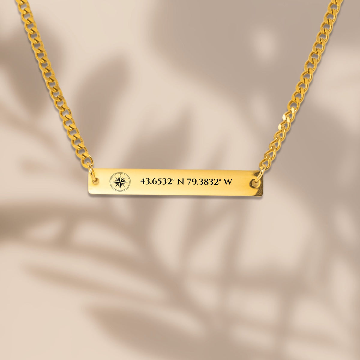 Compass rose coordinates bar on a Cuban chain in soft window light