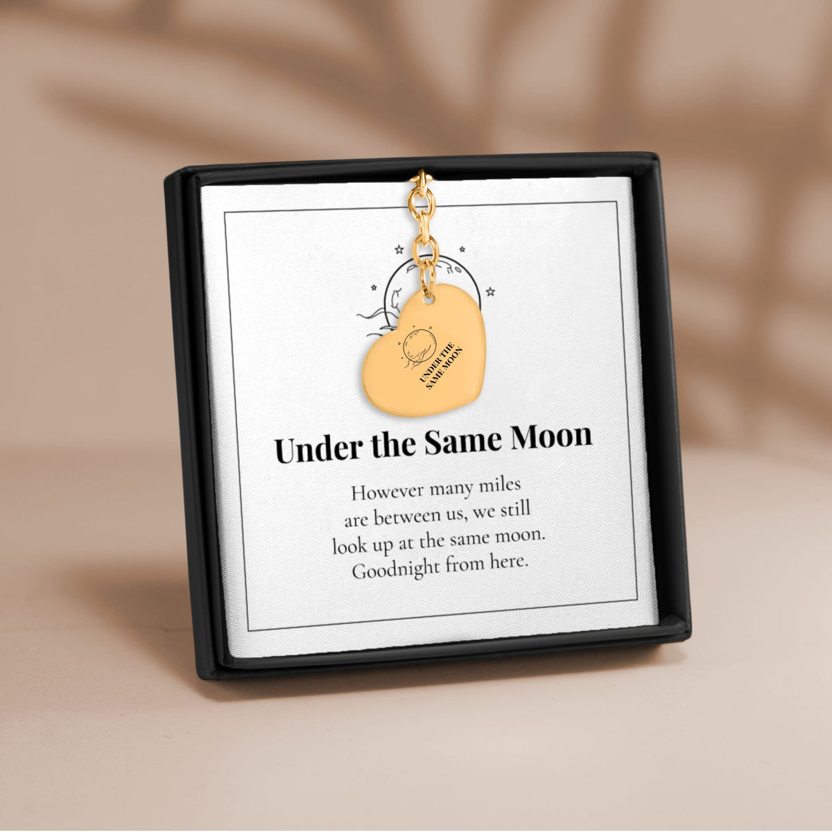 Under the Same Moon heart keychain in gold on its printed message card in a black gift box