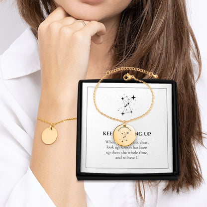 Keep Looking Up Orion coin bracelet worn on the wrist next to its gift box and message card