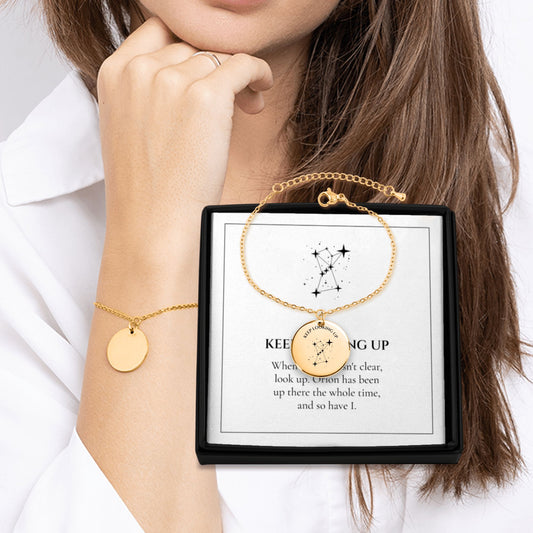 Keep Looking Up Orion coin bracelet worn on the wrist next to its gift box and message card