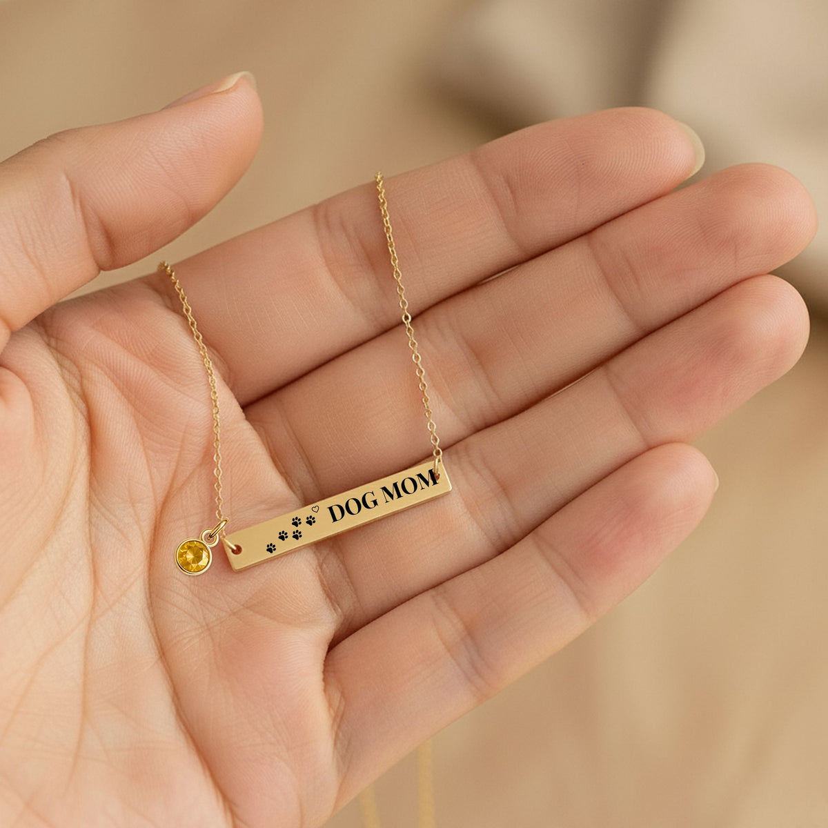 Bar pendant engraved with paw prints and DOG MOM held in an open hand