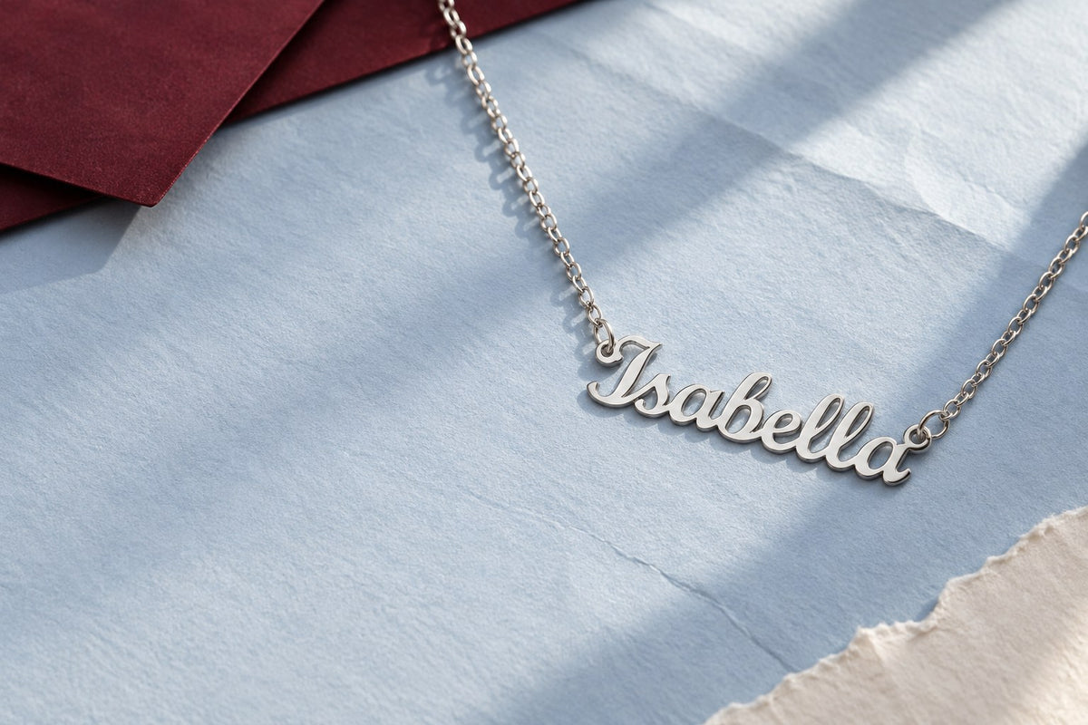 Silver script name necklace reading Isabella on pale blue paper